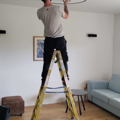 חשמלאי מתקין תאורה בתקרה בעזרת סולם וכלי עבודה