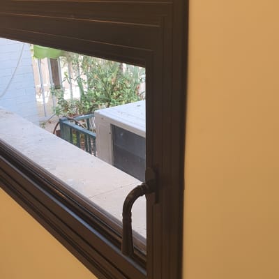 חלון אלומיניום עם ידית שחורה על קיר בהיר