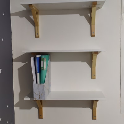 שלושה מדפים לבנים עם תומכים מעץ על קיר