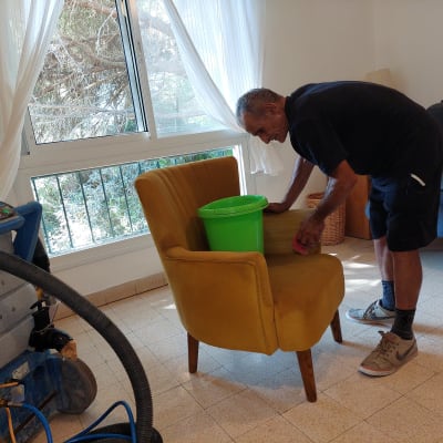 אדם מנקה כורסה עם דלי ירוק ומכונת ניקוי