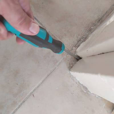 יד מחזיקה מברג בודקת חריץ ברצפה ליד קיר