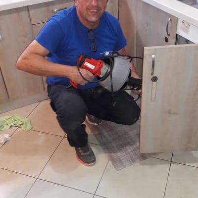 אדם מחזיק מכשיר אינסטלציה ליד ארון מטבח פתוח