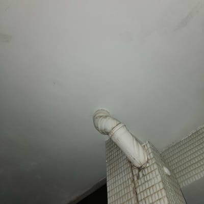 צינור לבן מחובר לקיר מרוצף באריחים קטנים