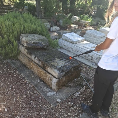 אדם מנקה מצבות בבית קברות עם צינור מים
