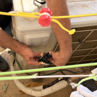 טכנאי מזגנים מתקן רכיבי חשמל וחיווט ביחידה החיצונית של המזגן