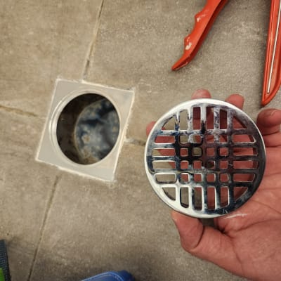 יד מחזיקה מכסה ניקוז מתכת ליד פתח ביוב פתוח