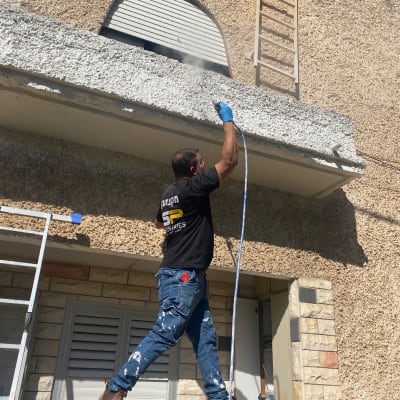 אדם צובע קיר חיצוני עם מכונת ריסוס צבע
