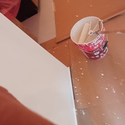 דלי צבע ורולר על רצפה מוגנת במהלך עבודת צביעת קיר
