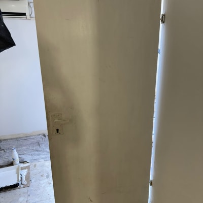 דלת לבנה עם ידית ומנעול, צבע ומברשת על הרצפה