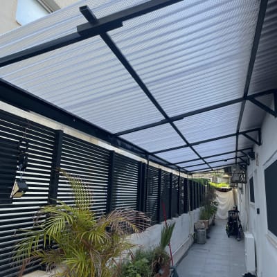 צמחים בעציצים לאורך שביל מרוצף עם גג שקוף