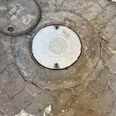 מכסה ביוב על מדרכה עם לכלוך מסביב