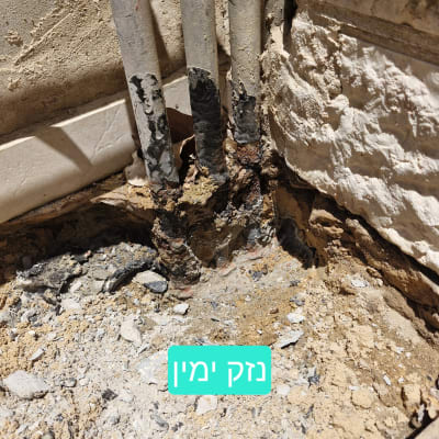 צינורות חלודים ליד קיר עם חול ואבנים