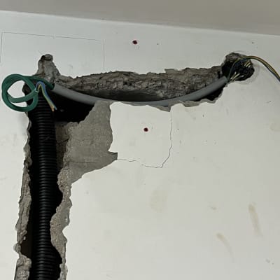 כבלים חשמליים יוצאים מקיר שבור עם צינור שחור