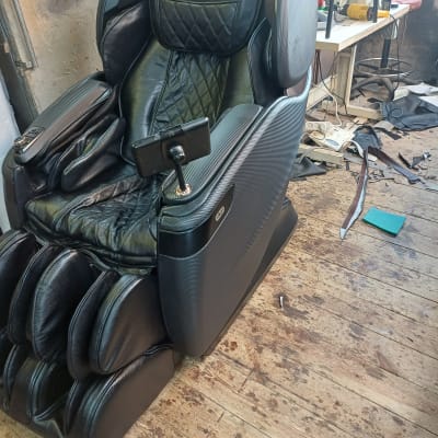 כיסא עיסוי שחור עם מכונת תפירה ברקע