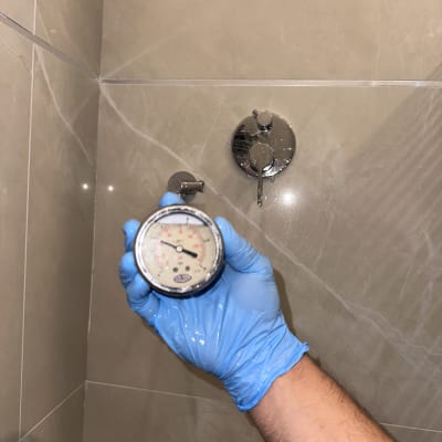 מד לחץ מים מוחזק ביד עם כפפה כחולה במקלחת