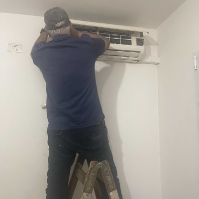 אדם על סולם מתקין מזגן על קיר לבן