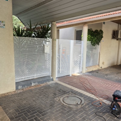 שער מתכת לבן עם צמחייה ברקע וחוט חשמל על הקרקע