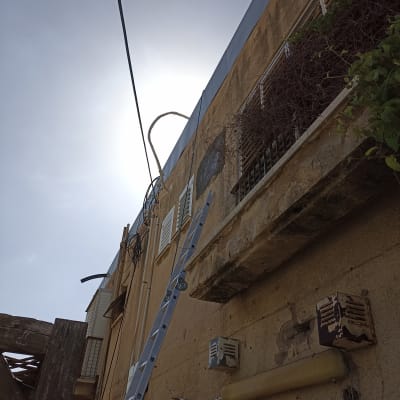 סולם מתכת נשען על קיר בניין עם צינורות חשמל