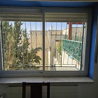 חלון עם סורגים ונוף חיצוני של בניינים ועצים