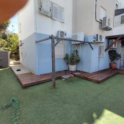 חצר עם דק עץ, צמחייה ומזגנים על קיר