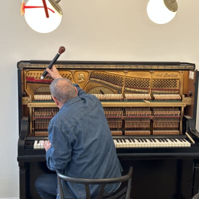 אדם מכוון פסנתר עם כלי כיוון בידו