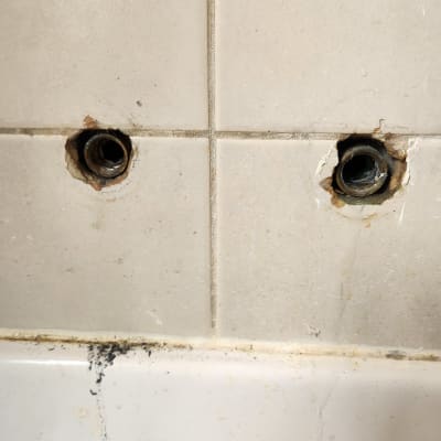 שני חורים בקיר קרמיקה עם צינורות חשופים