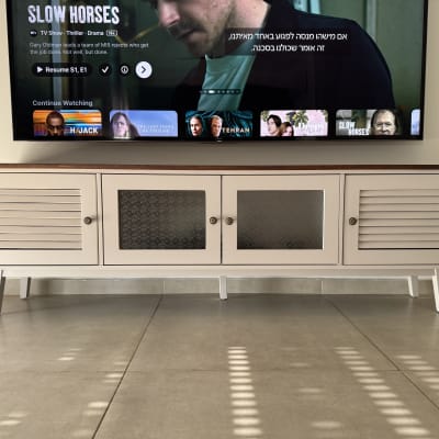 שידת טלוויזיה לבנה עם דלתות זכוכית ומסך טלוויזיה מעליה