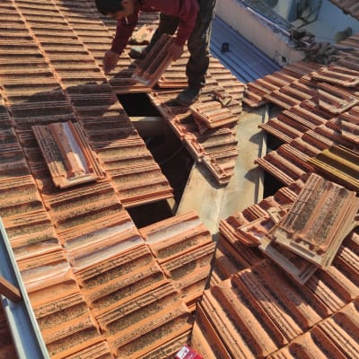 עובד מתקין רעפים על גג רעפים אדום