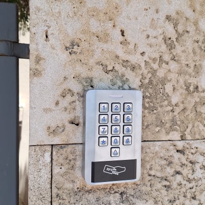 התקנת קודן כסוף עם קורא קרבה על קיר אבן לצד שער