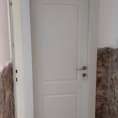 דלת לבנה עם ידית מתכת וקיר אבן בצד