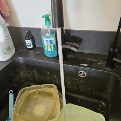 ברז מים זורמים בכיור מטבח עם כלים מלוכלכים