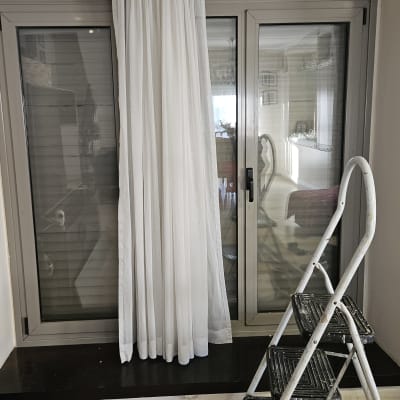 תריסים סגורים מאחורי וילון לבן ליד חלון זכוכית