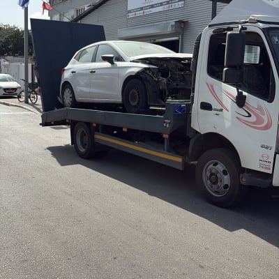 רכב על גרר מול מוסך עם שלט בעברית