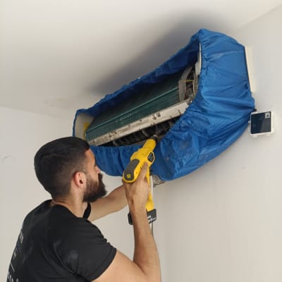 אדם מנקה מזגן עם מכשיר ניקוי צהוב