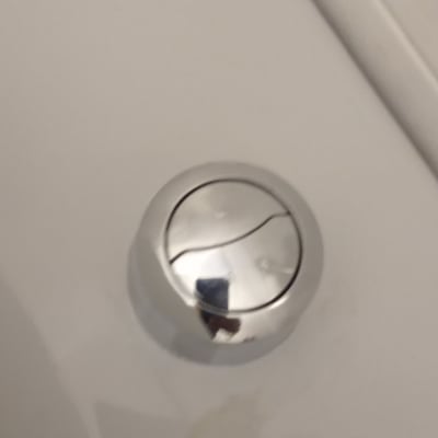 לחצן ניאגרה כסוף על מכסה אסלה לבן