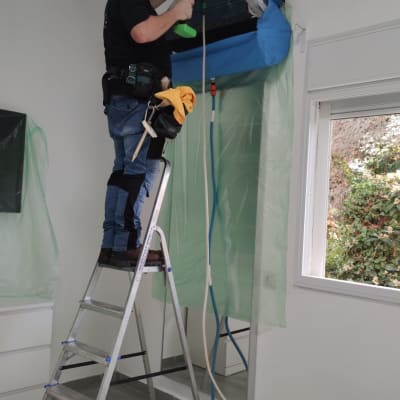 טכנאי על סולם מתקין מזגן עם כלים