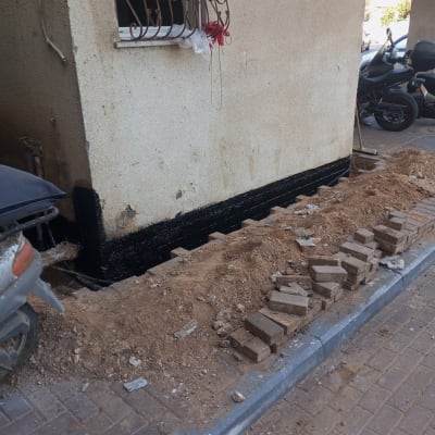 קיר עם איטום שחור בתחתית, ערימת לבנים ועפר