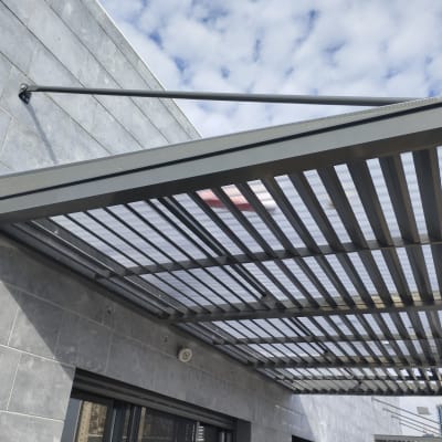 פרגולה מתכתית עם גג שקוף על קיר חיצוני