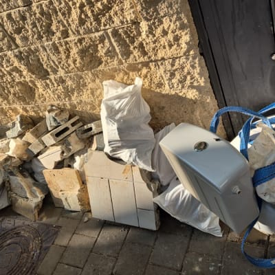 שקיות פסולת, בלוקים, אריחים, מיכל שירותים ליד קיר אבן