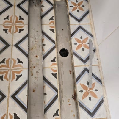 תעלת ניקוז פתוחה עם מכסה מתכת חלוד על רצפה מעוטרת