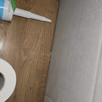 אקדח סיליקון ורצפת עץ ליד קיר אריחים