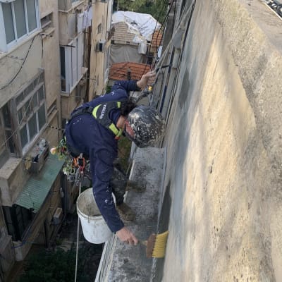 אדם מנקה קיר חיצוני עם מברשת וחבל בטיחות