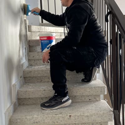 אדם צובע קיר במדרגות עם מברשת ודלי צבע