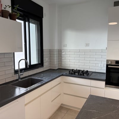 מטבח משופץ עם ארונות לבנים ומשטח עבודה כהה