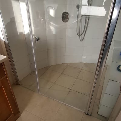 מקלחון זכוכית עם ראש מקלחת מתכת על קיר לבן