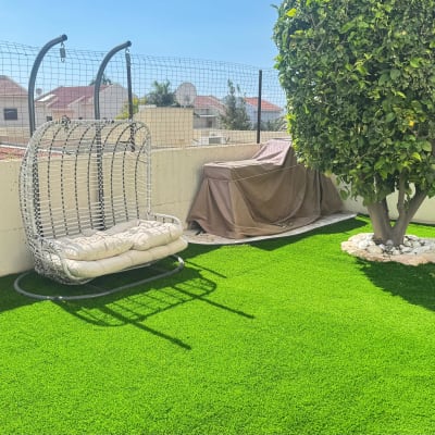 דשא סינטטי עם נדנדה ועץ בגינה