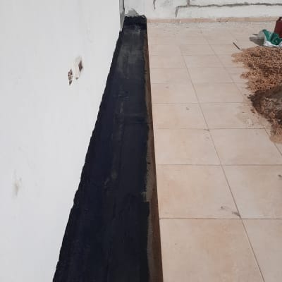 איטום קיר עם חומר שחור ליד רצפה מרוצפת