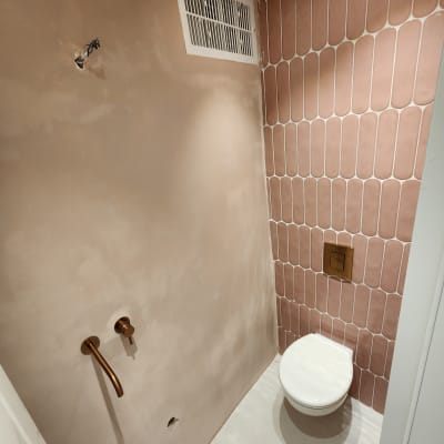 חדר שירותים עם קיר אריחים ורודים וברזים מותקנים
