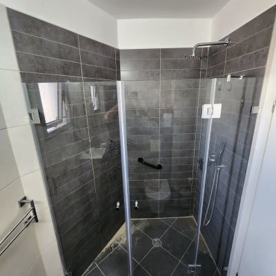 מקלחון זכוכית עם ראש מקלחת וקיר אריחים אפור