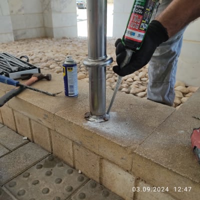אדם מתקין עמוד מתכת עם חומר איטום על קיר לבנים